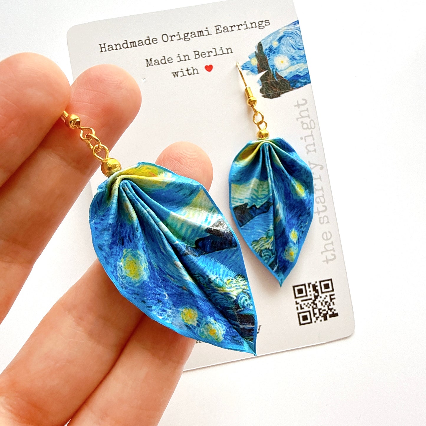 Handmade origami earrings inspired by Van Gogh's 'Starry Night' held against a card with product details.