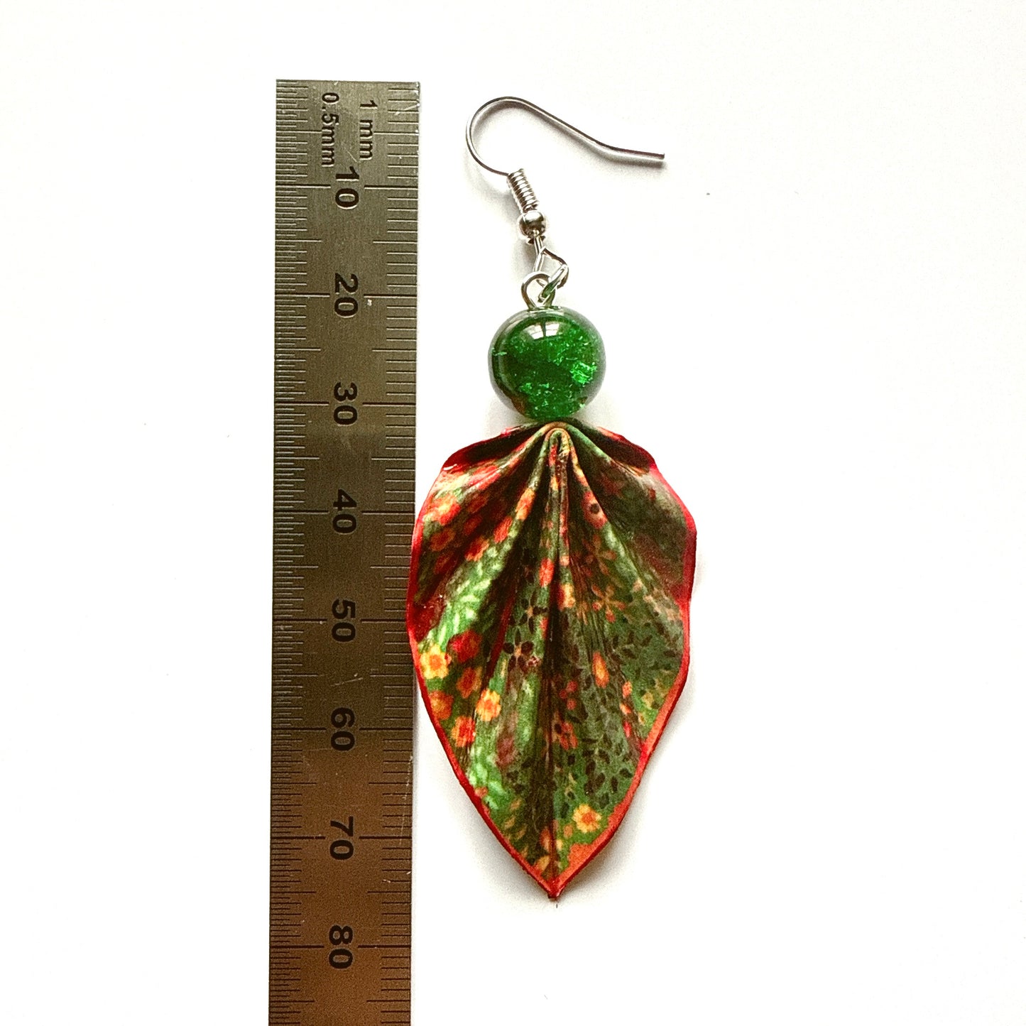 Leaf-shaped earrings with a green gemstone on a white background with a ruler for scale.