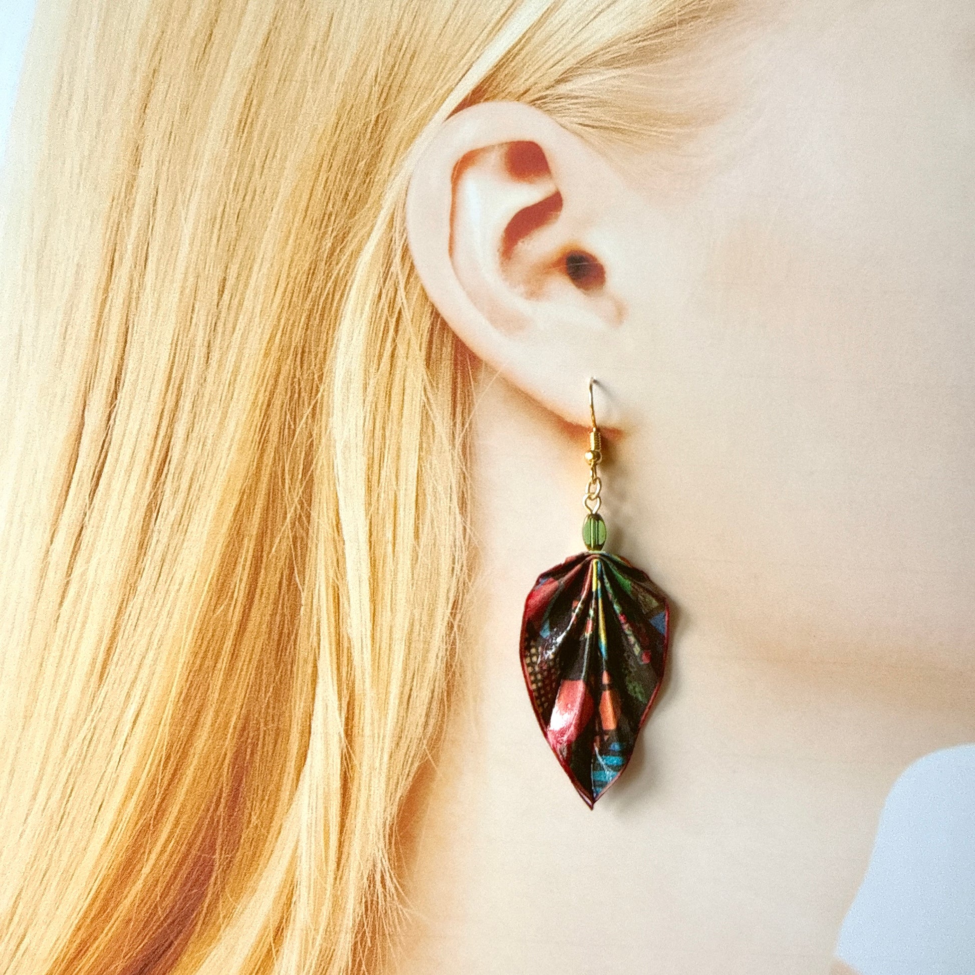 Close-up of a person wearing a colorful leaf-shaped earring with blonde hair.