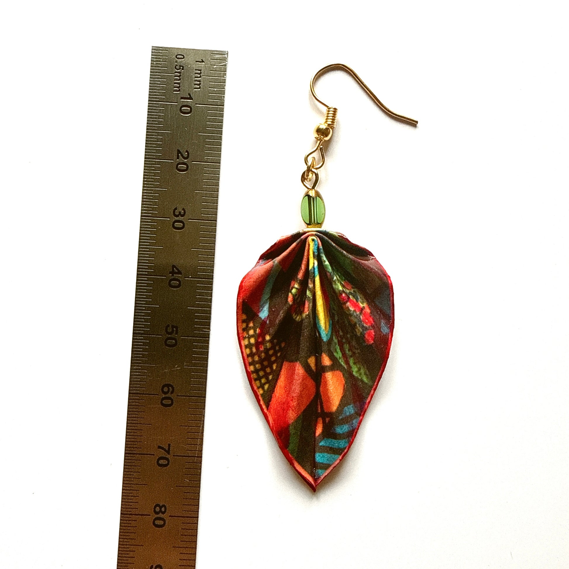 Colorful leaf-shaped earring next to a ruler on a white background