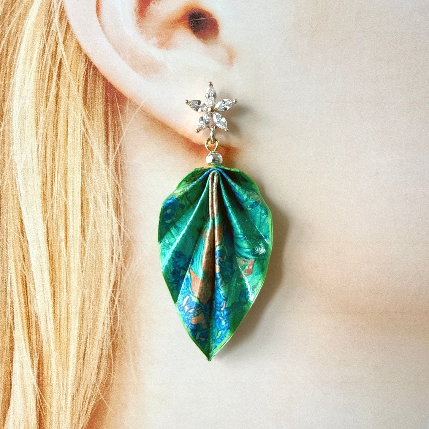Green leaf-shaped earring worn by a person with blonde hair.