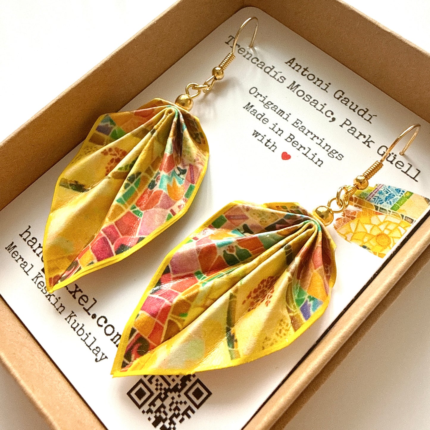 Colorful origami earrings in a box with a card about Antoni Gaudi.