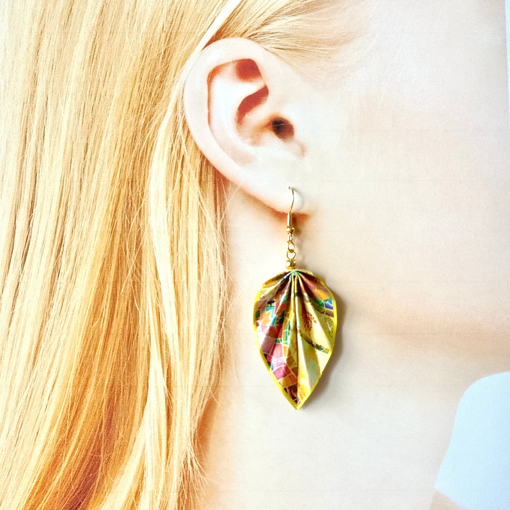 Gold leaf-shaped earring worn by a person with blonde hair.