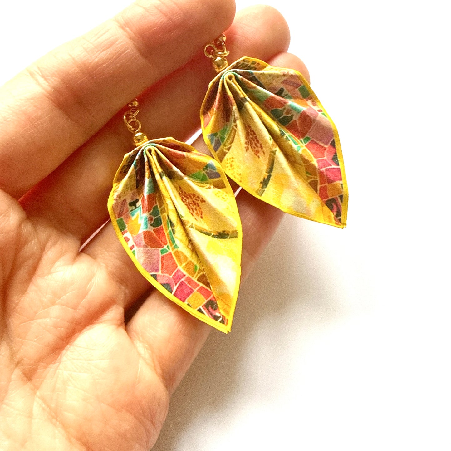 Colorful leaf-shaped earrings held in a hand against a white background