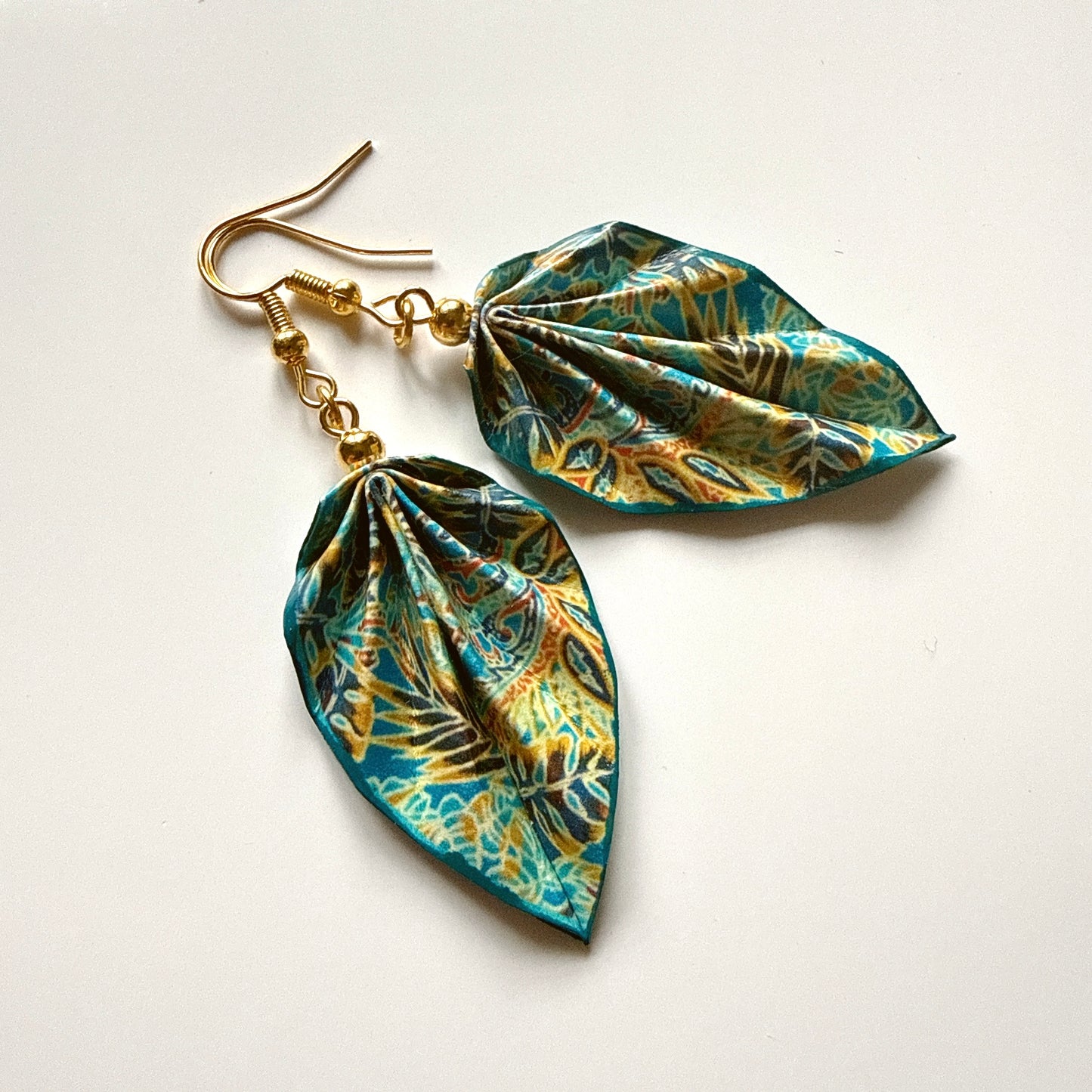 Leaf-shaped earrings with gold hooks on a white background