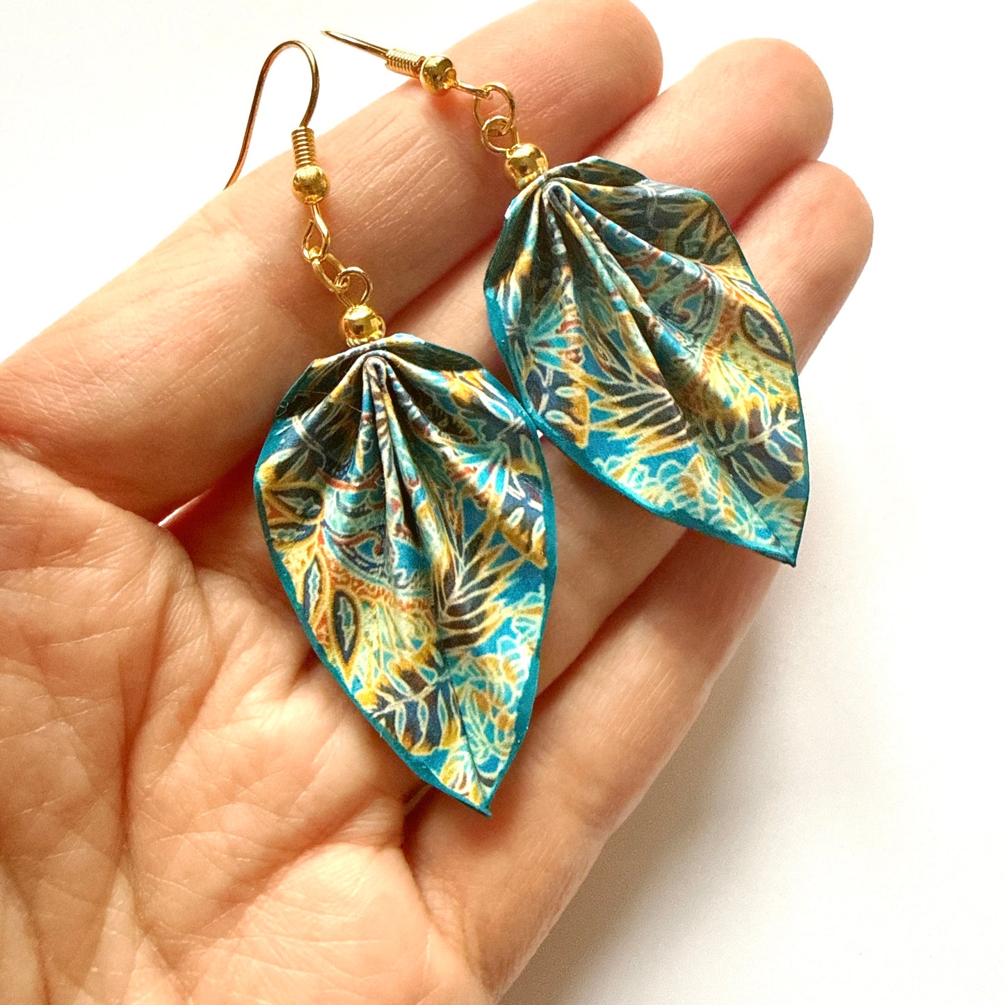 Leaf-shaped earrings with a colorful pattern held in a hand against a white background