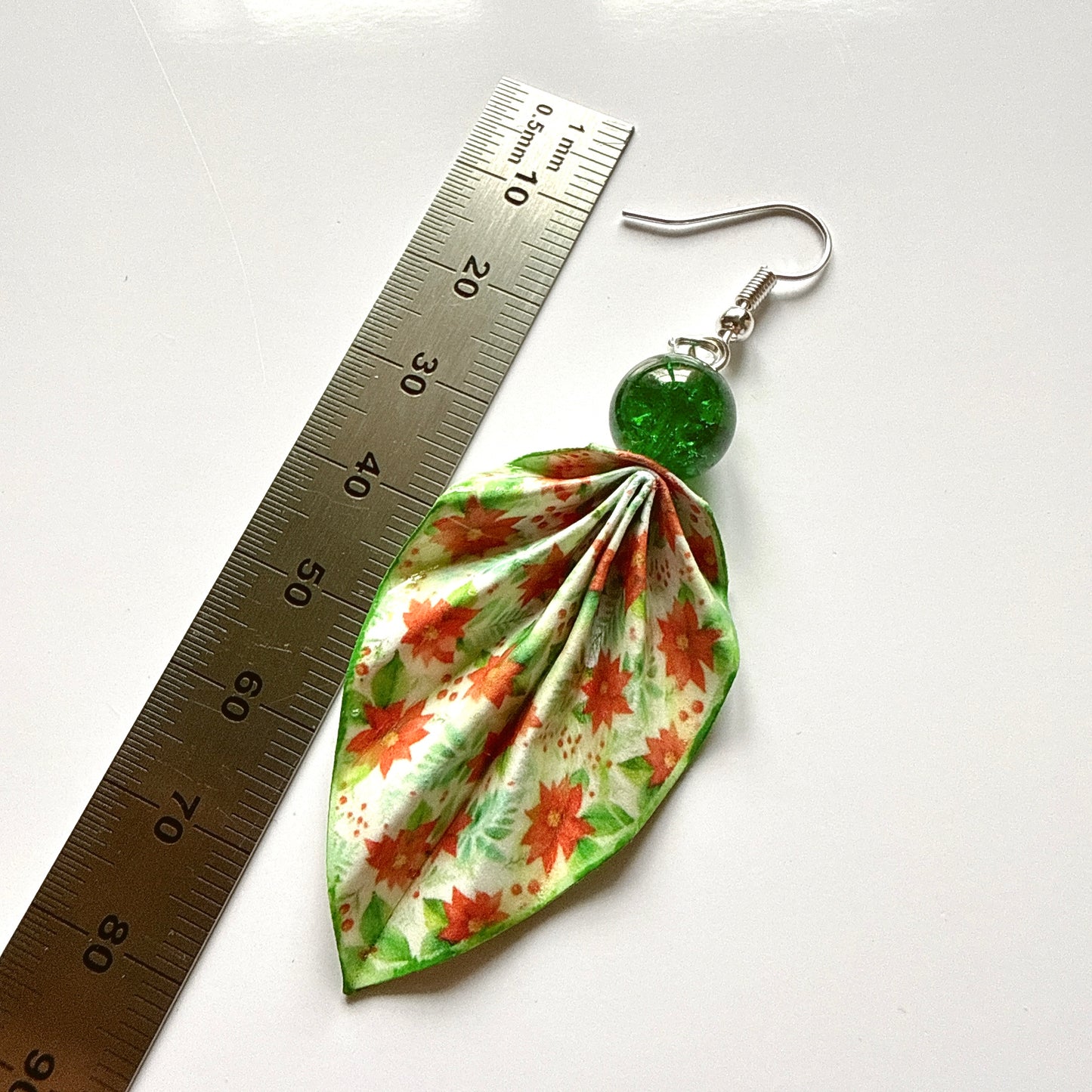 Floral earring with green bead next to a ruler on a white background