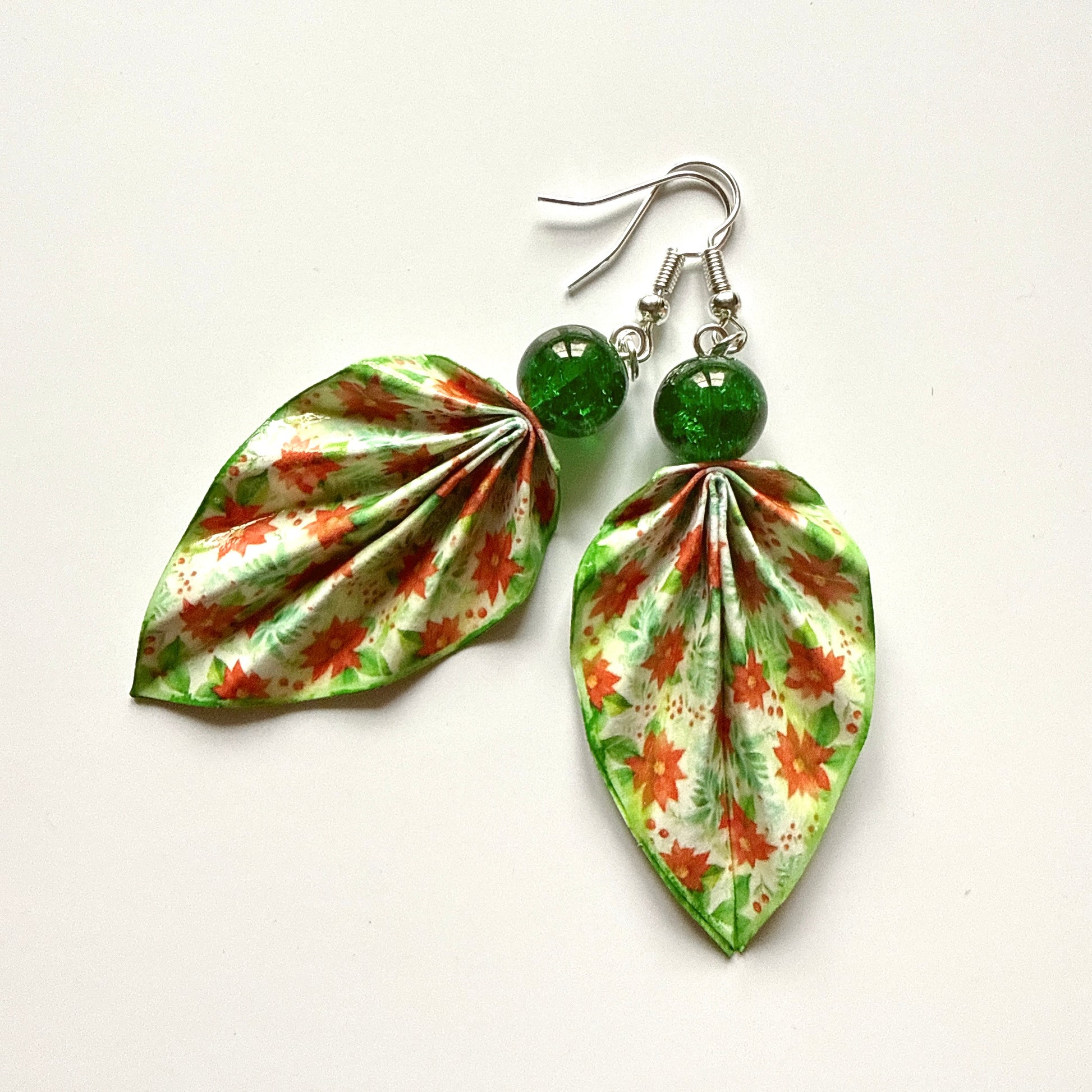 Leaf-shaped earrings with floral pattern and green beads on a white background