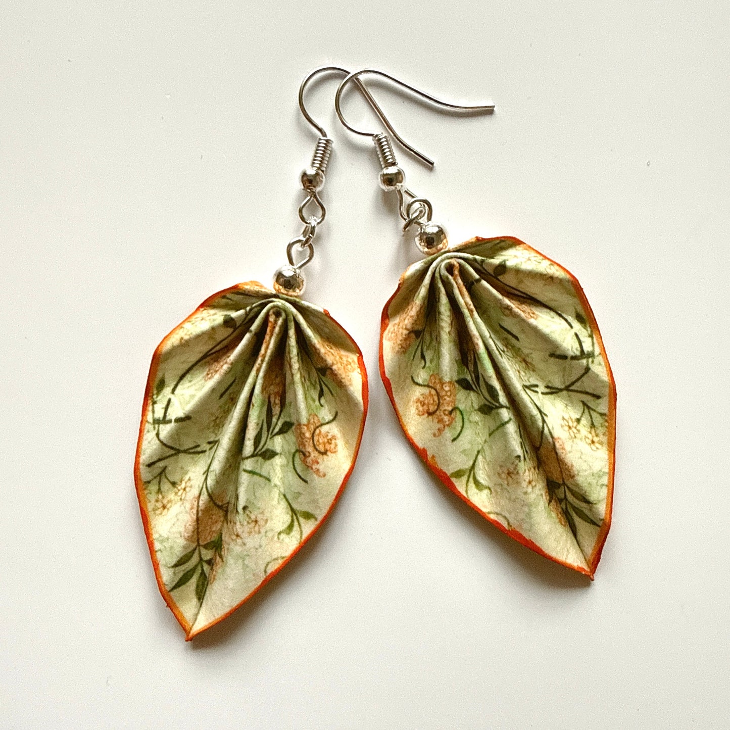 Pair of leaf-shaped earrings with floral pattern on a white background