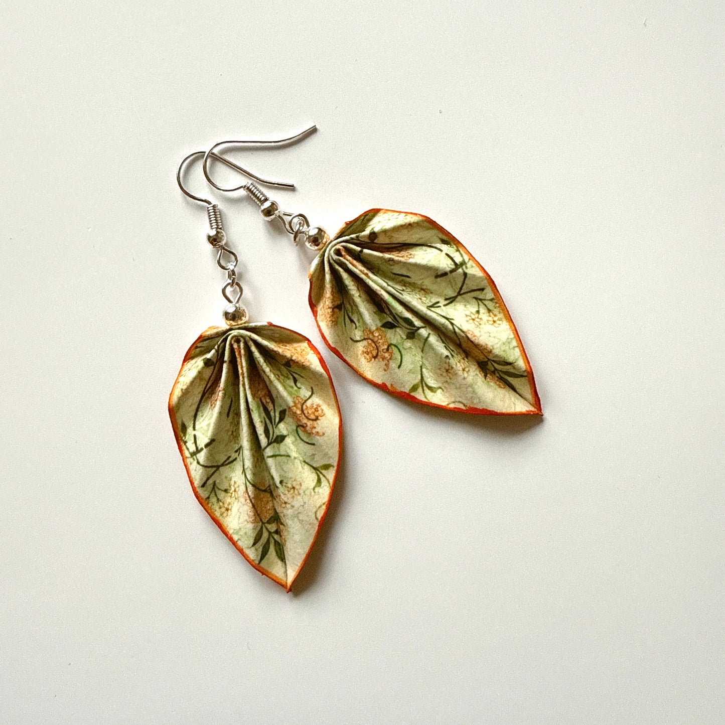 Pair of leaf-shaped earrings with floral patterns on a white background