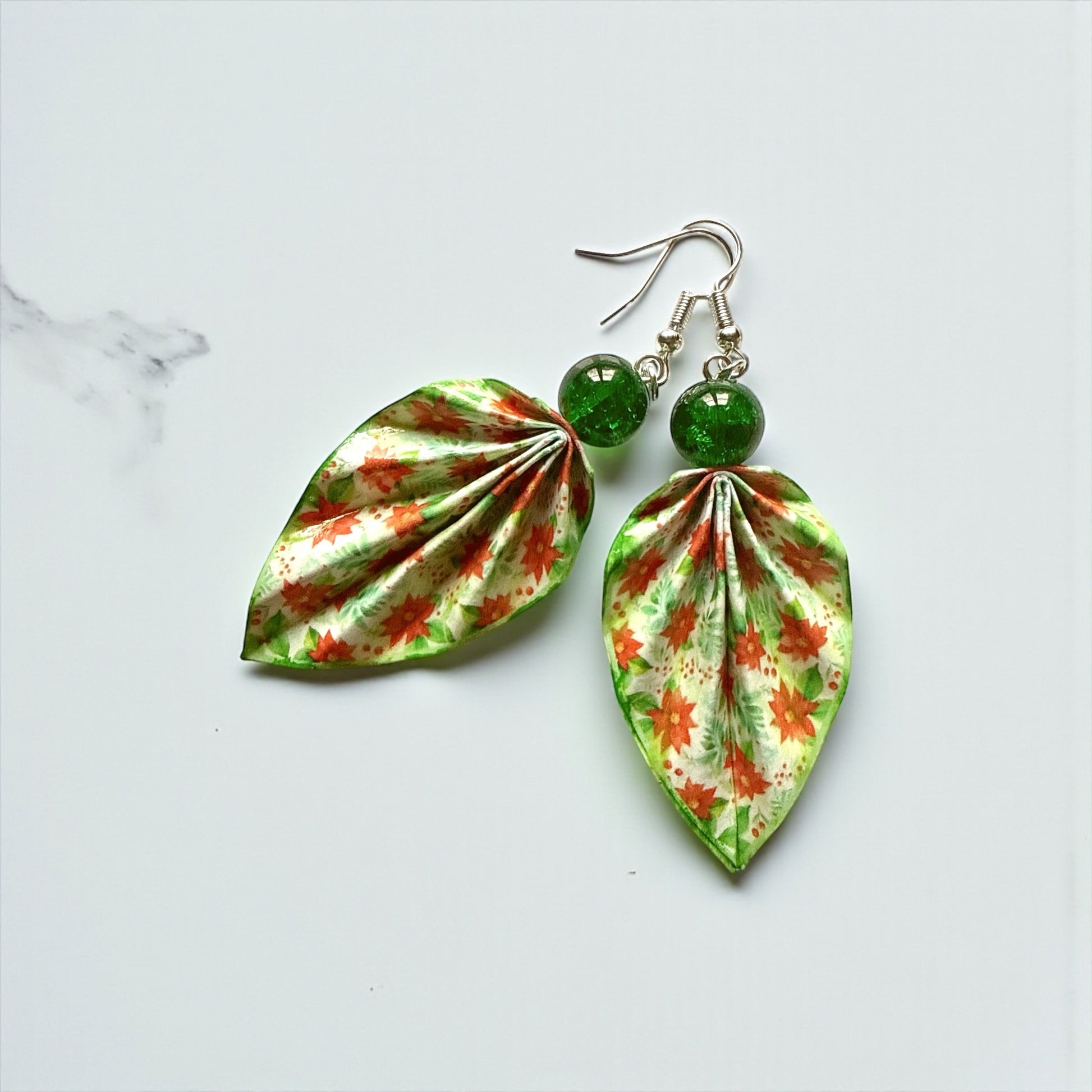 Leaf-shaped earrings with floral pattern and green beads on a light gray background