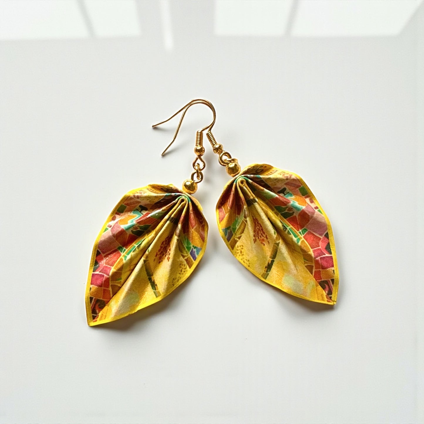 Gold leaf-shaped earrings with colorful patterns on a white background