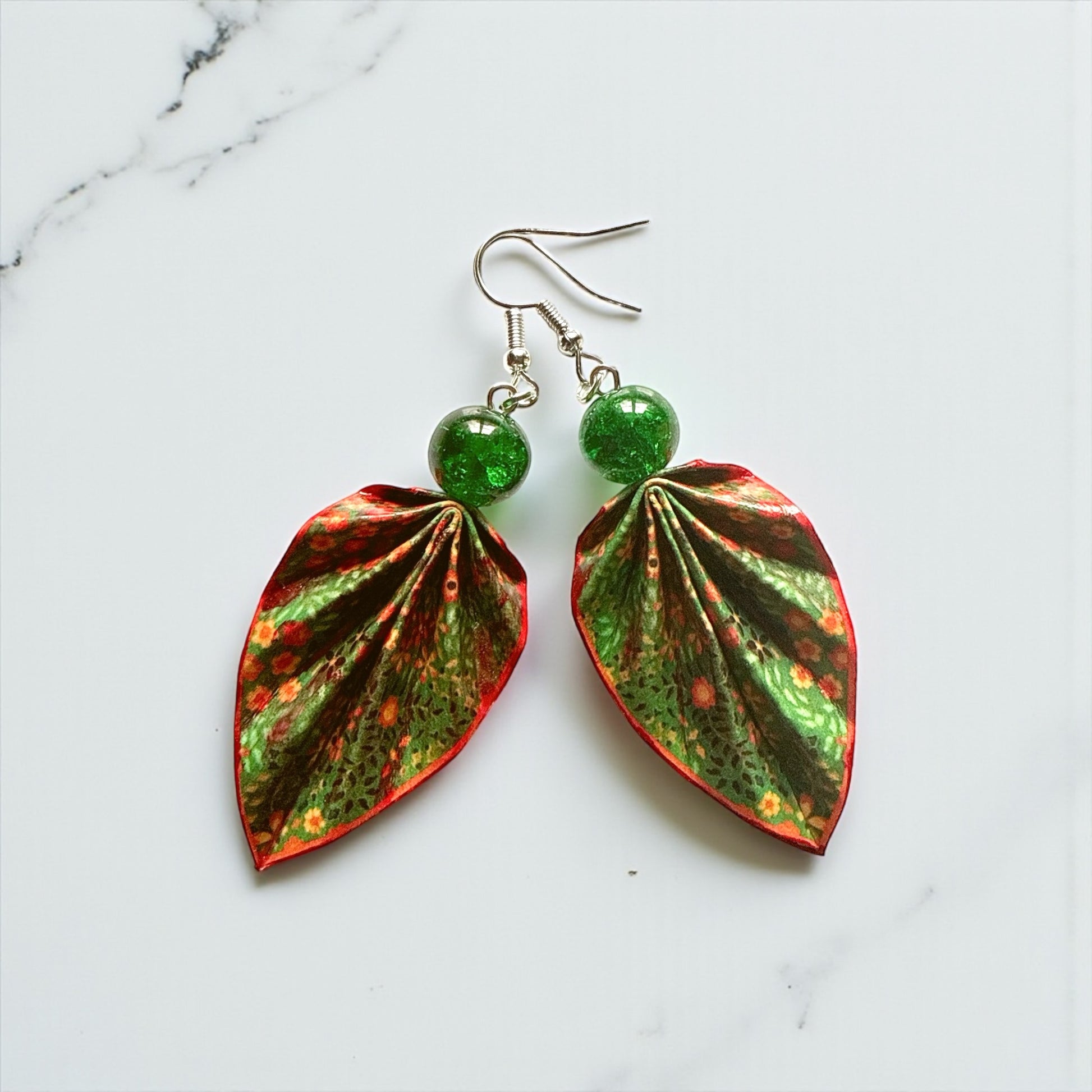 Leaf-shaped earrings with green gemstones on a marble background